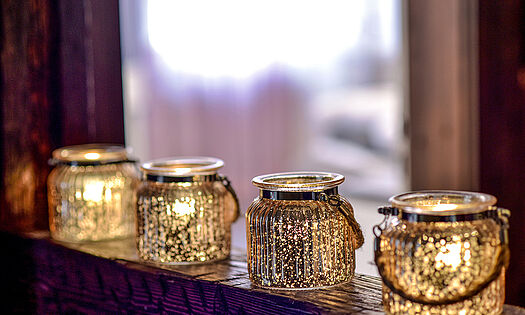 Eine Reihe an brennenden Kerzen in farbigen Gläsern